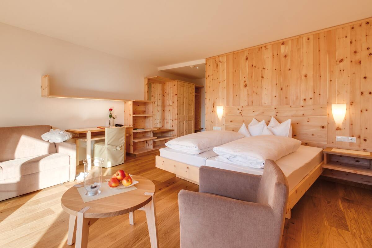 Une pièce meublée de meubles en bois, avec un lit, un canapé, une petite table sur laquelle se trouvent des pommes et une chaise.