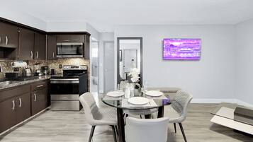 Una cocina moderna con armarios oscuros, un microondas y una estufa. Hay un comedor con una mesa de vidrio y sillas.