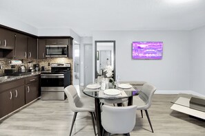 A modern kitchen with dark cabinets, a microwave, and a stove. There is a dining area with a glass table and chairs.