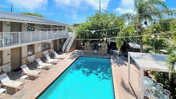 Zona de piscina con sillones de descanso, una escalera y un edificio con balcón.