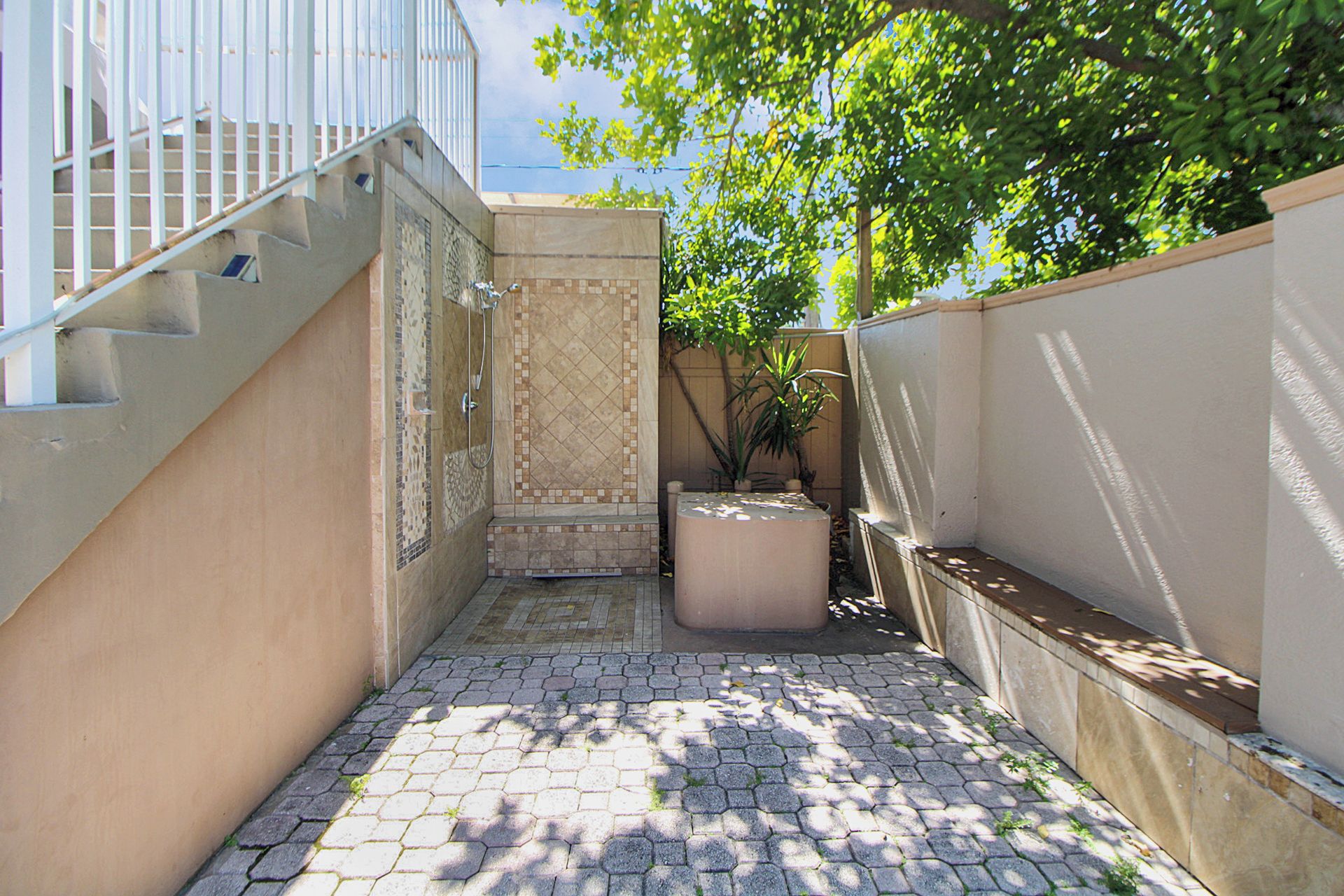 A narrow outdoor corridor with a tiled floor, a small seating area, and a staircase leading to an upper level.