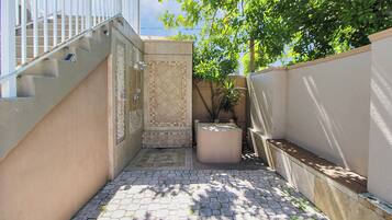A narrow outdoor corridor with a tiled floor, a small seating area, and a staircase leading to an upper level.