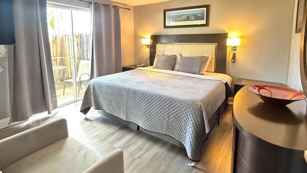 Hotellihuone, jossa on sänky, työpöytä, tuoli ja suuri ikkuna, jossa on verhot.