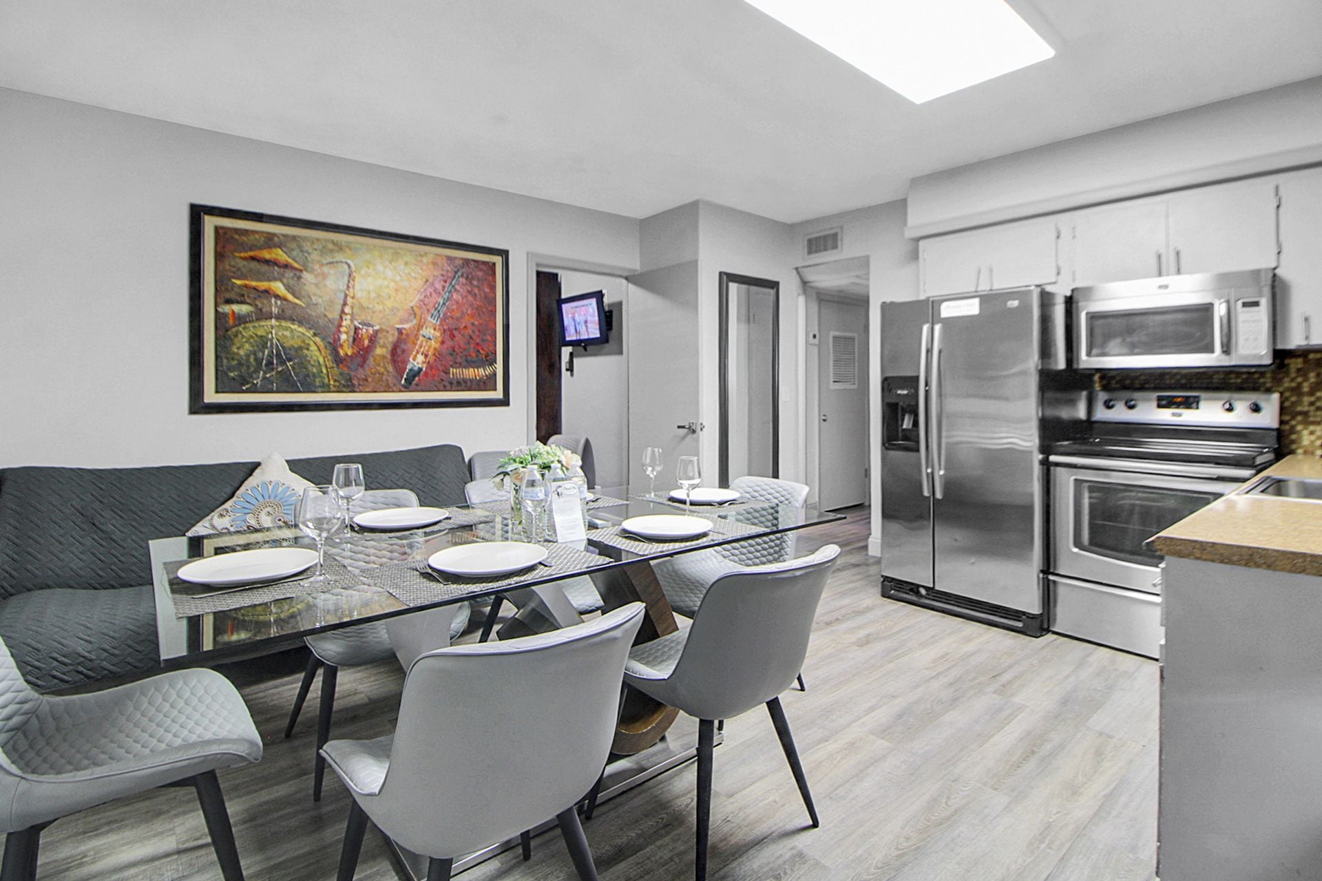 A modern kitchen with stainless steel appliances, a dining area with a glass table and chairs, and a painting on the wall.