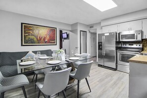 A modern kitchen with stainless steel appliances, a dining area with a glass table and chairs, and a painting on the wall. - Sheridan Suites Apartments Hotel (Dania Beach)