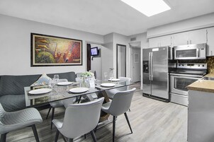 Een moderne keuken met roestvrijstalen apparatuur, een eethoek met een glazen tafel en stoelen, en een schilderij aan de muur.