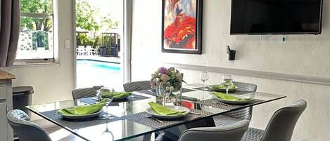 A modern dining area with a glass table, grey upholstered chairs, and a painting on the wall.