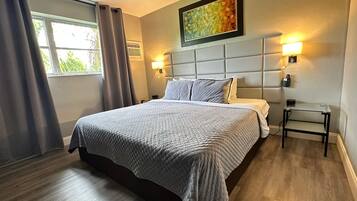 Quarto de hotel moderno com uma cama grande, duas luminárias de cabeceira, um quadro sobre a cama e uma mesinha com uma luminária.