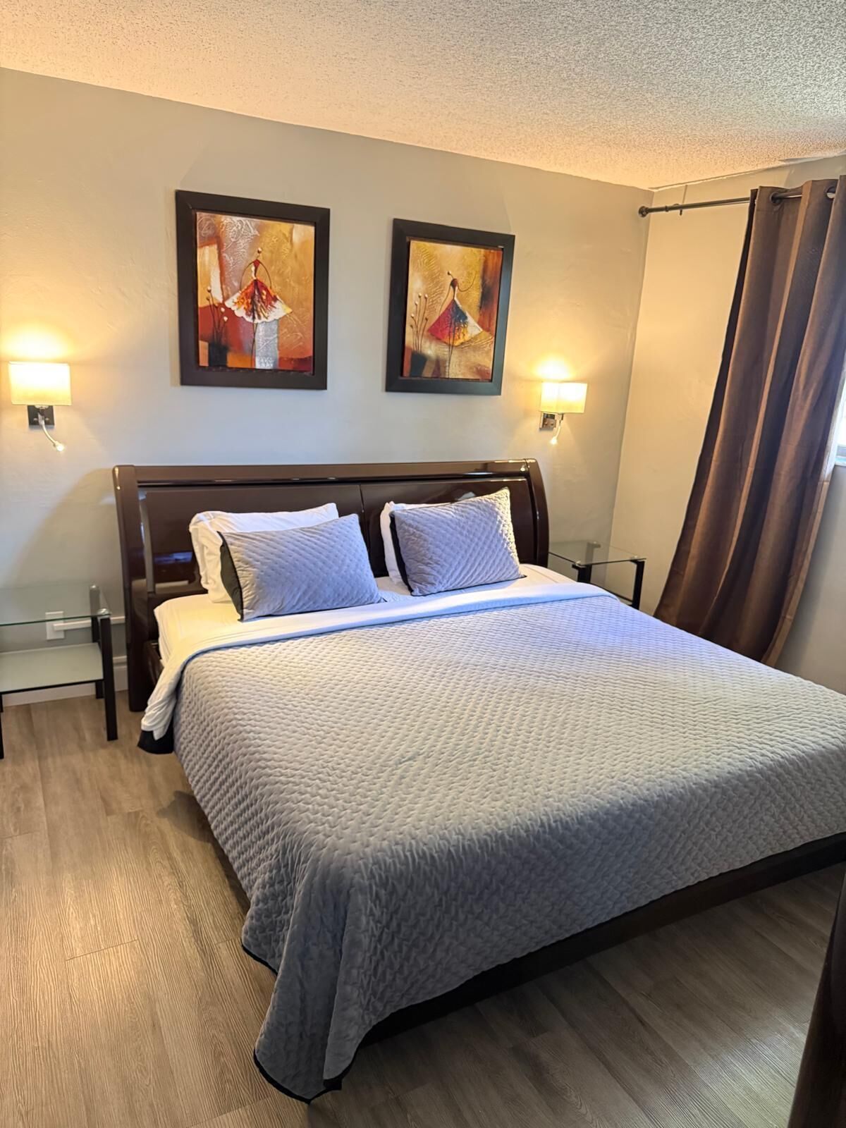 A hotel room with a bed, two wall-mounted lamps, and two framed artworks on the wall.