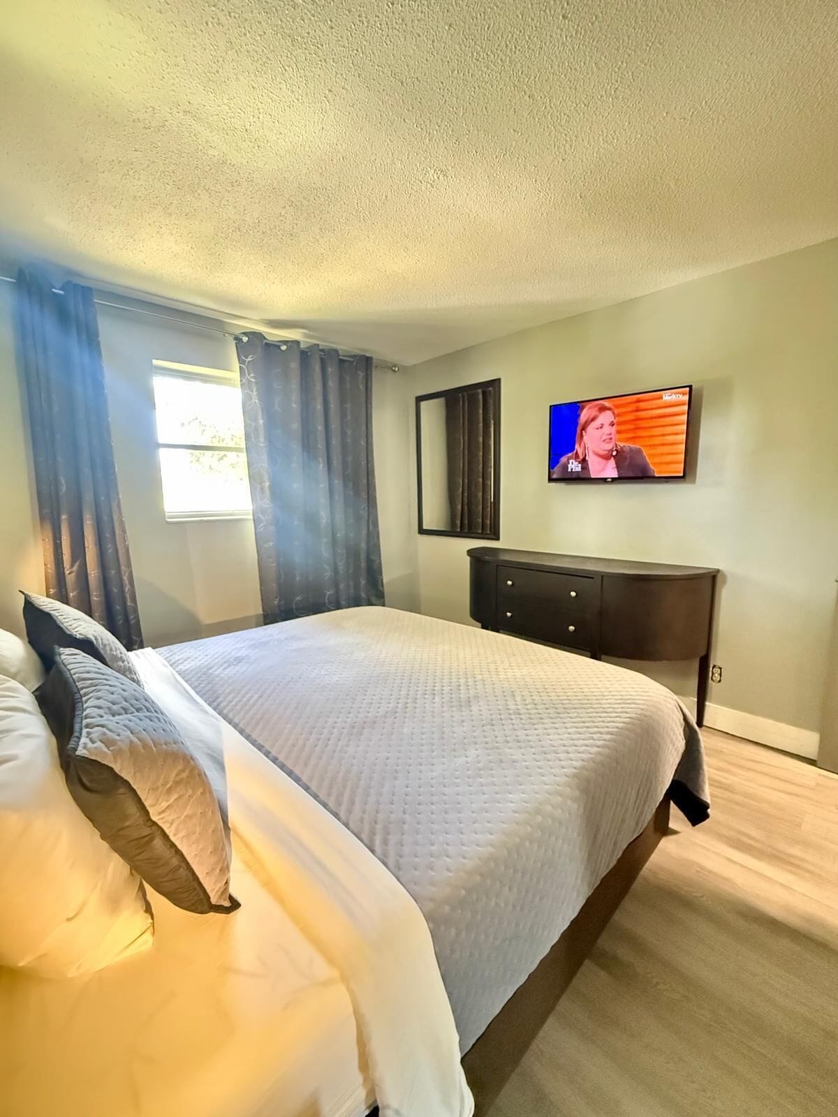 A bedroom with a bed, a TV, a dresser, and a window with curtains.