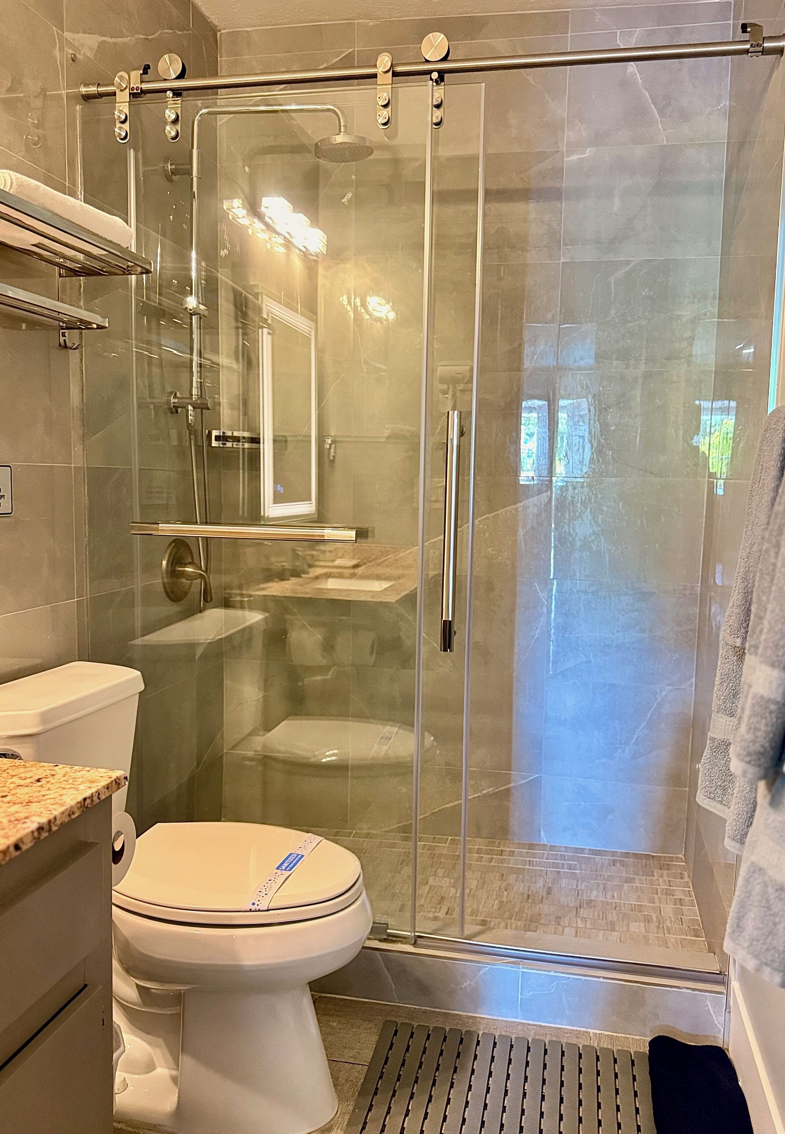 Un baño moderno con ducha de mampara de vidrio, inodoro y lavamanos.