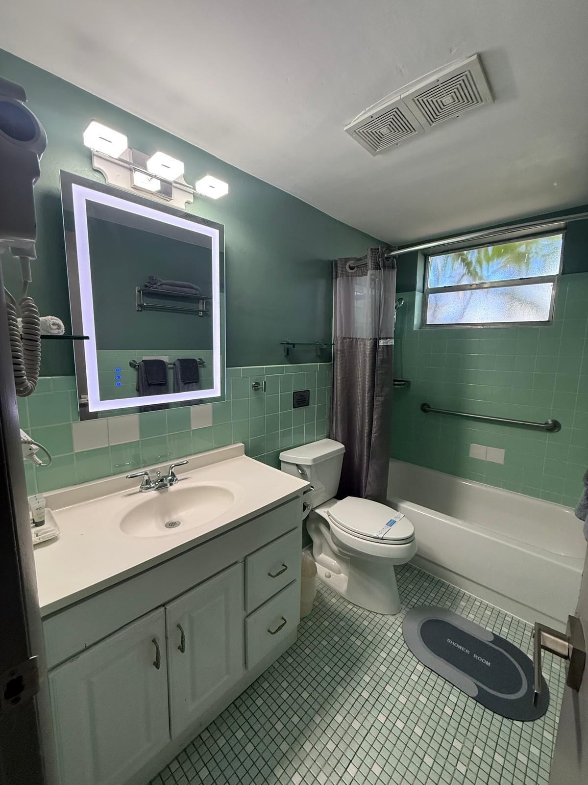 Un baño con lavamanos, inodoro y bañera. Incluye un tapete para ducha y un perchero para toallas.