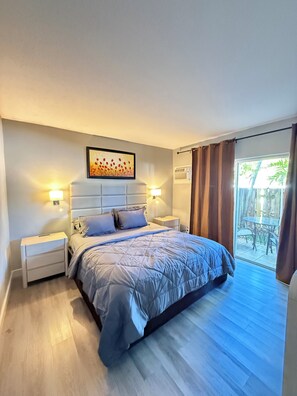 Un dormitorio con cama, mesitas de noche, cabecera y vistas al exterior.