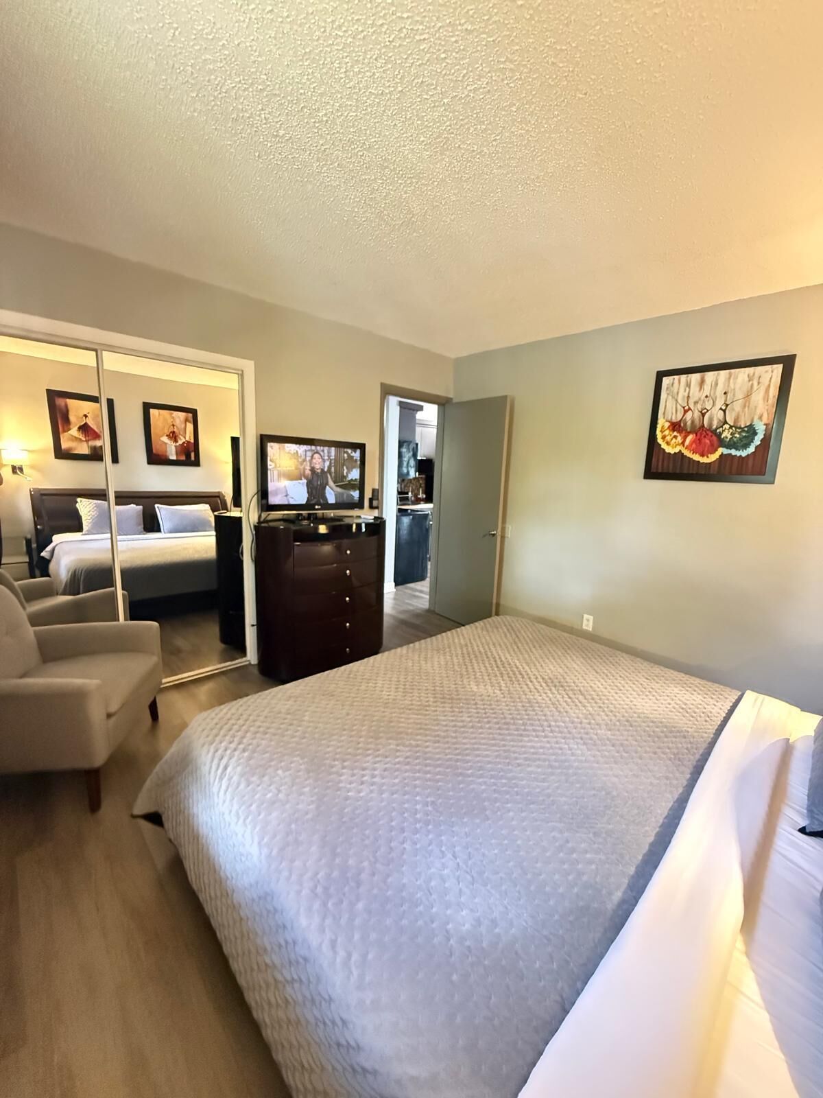 A hotel room with a large bed, a desk, a chair, a television, and a door leading to a bathroom.