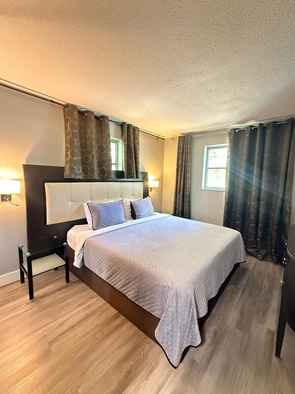 A hotel room with a large bed, a bedside table, a nightstand, and a window with curtains.