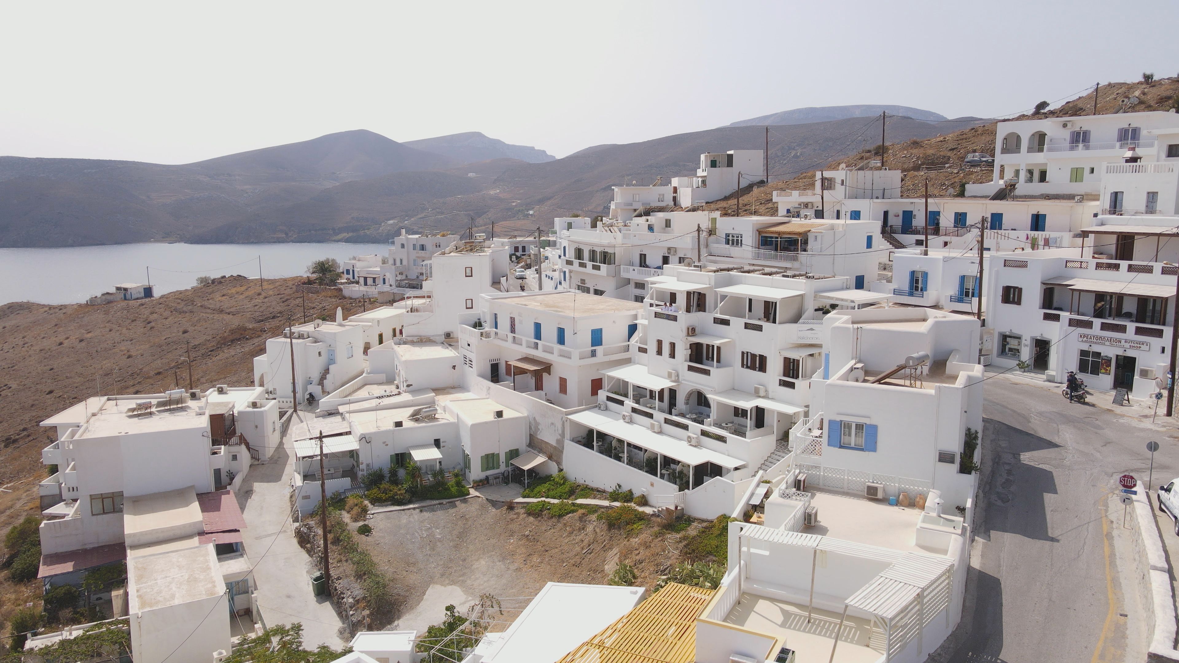 A coastal village with white buildings, a clear view of the sea, and a hilly backdrop.