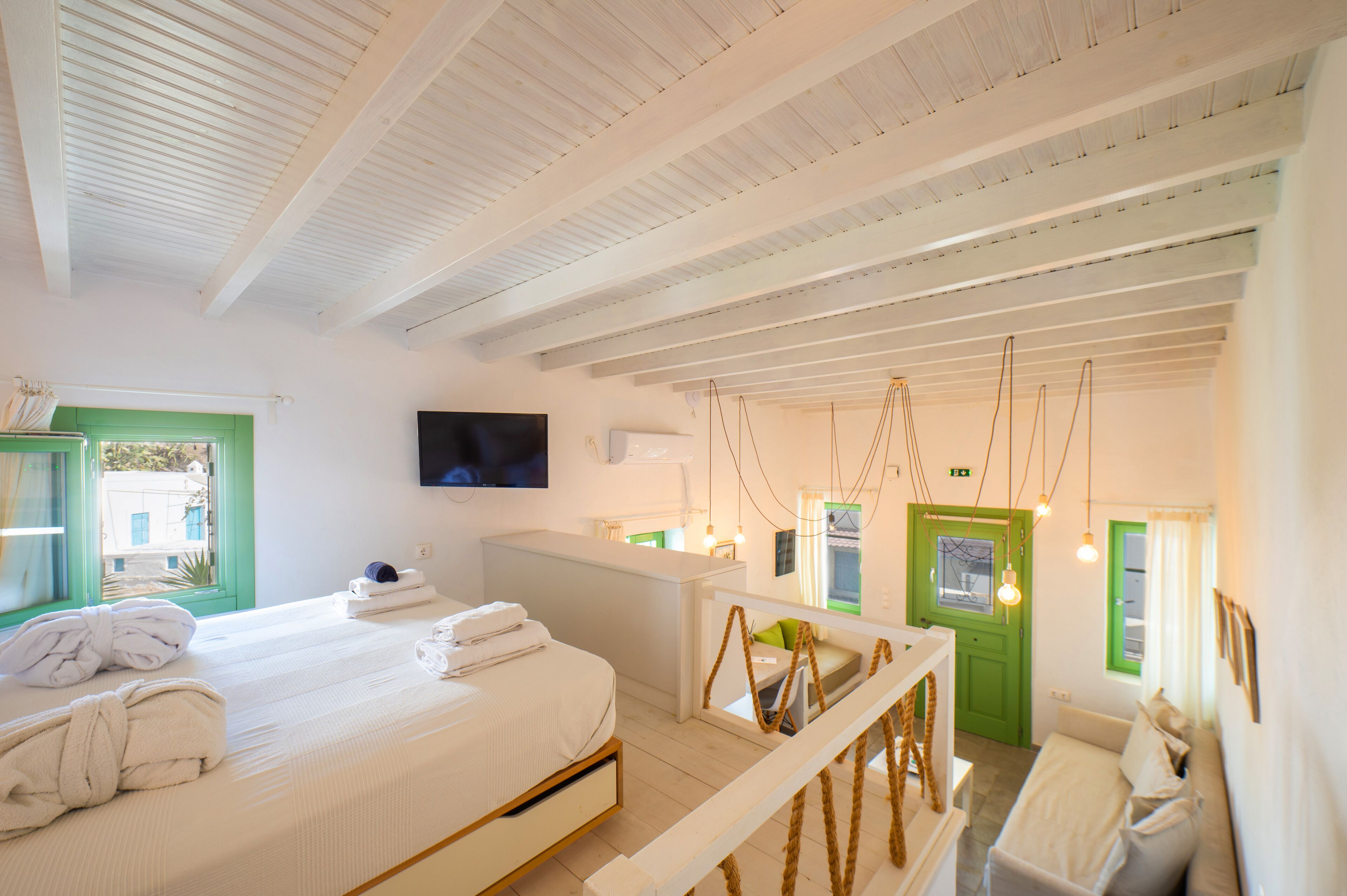 A hotel room with a bed, a green door, a white desk, and a TV mounted on the wall.