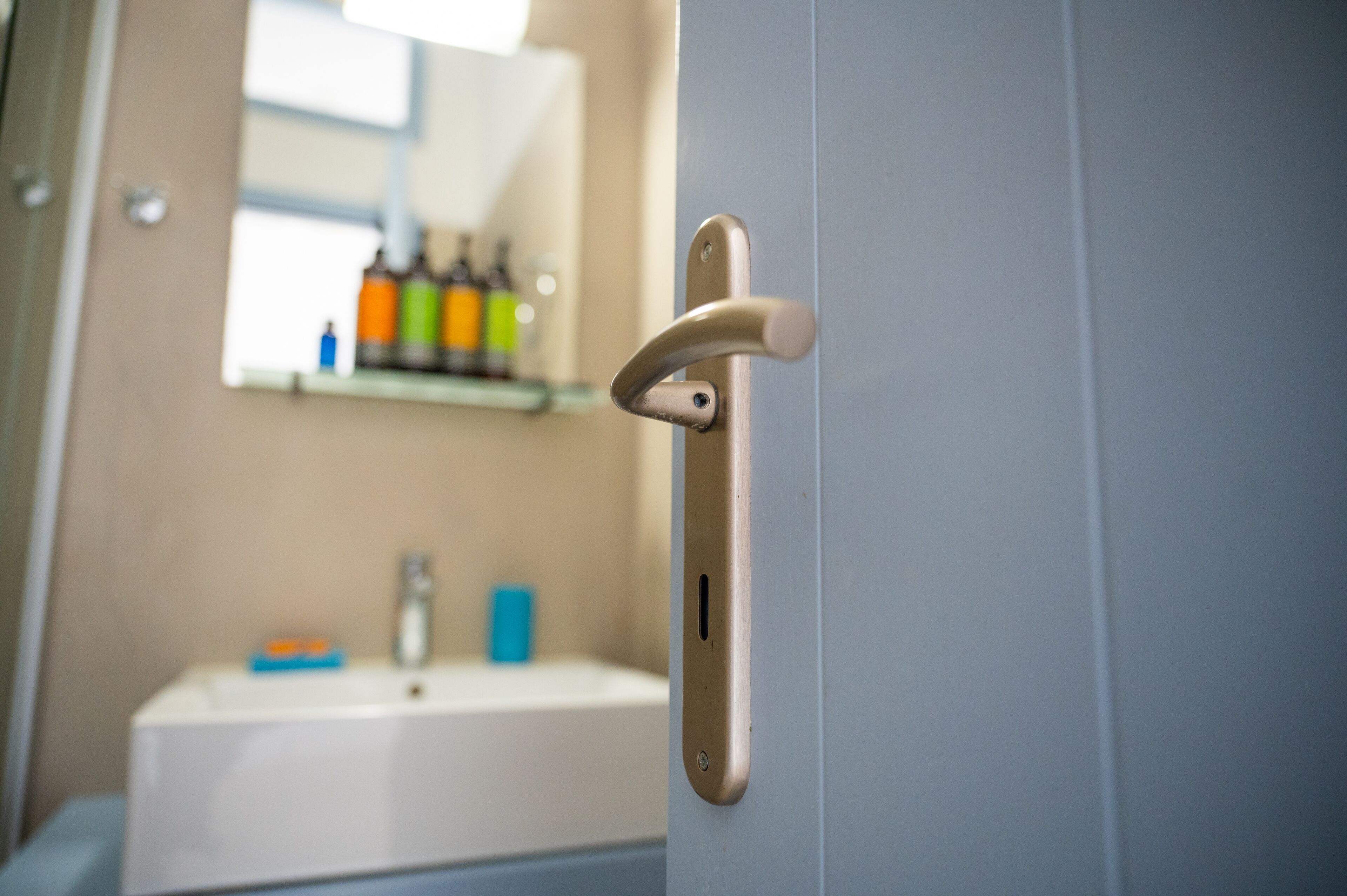 A bathroom with a sink, mirror, and toiletries on a shelf.