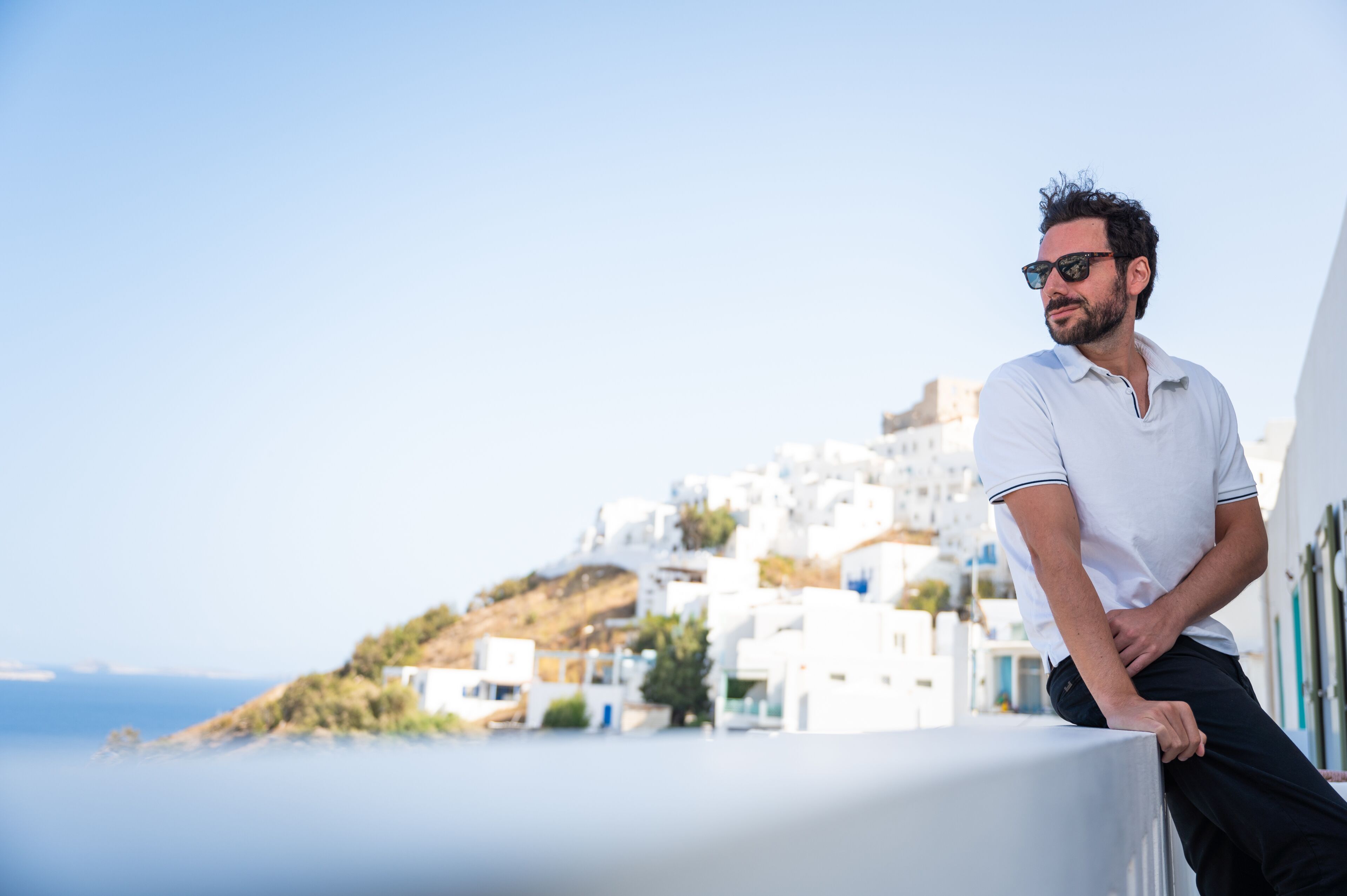 A man leaning on a balcony with a view of white buildings and a hillside.