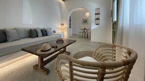 A modern living room with a sofa, a wooden coffee table, and a wicker chair. - Kallichoron Art Hotel (Astypalaia)