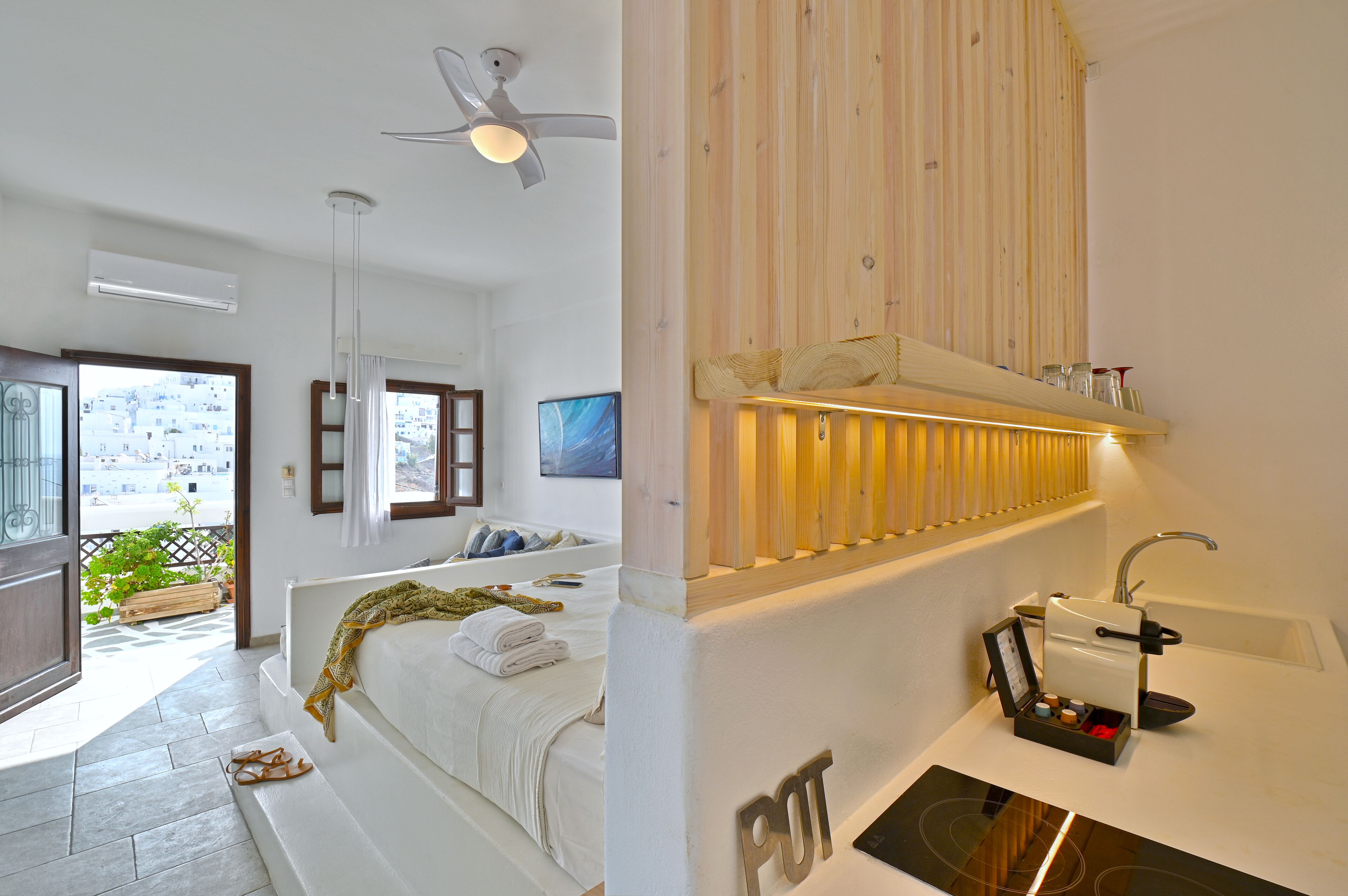 A modern hotel room with a bed, a bathroom with a sink and a coffee machine, and a balcony with a view of buildings.