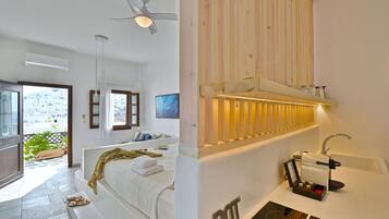 Habitación de hotel moderna con cama, baño con lavamanos y cafetera, y balcón con vistas a edificios.