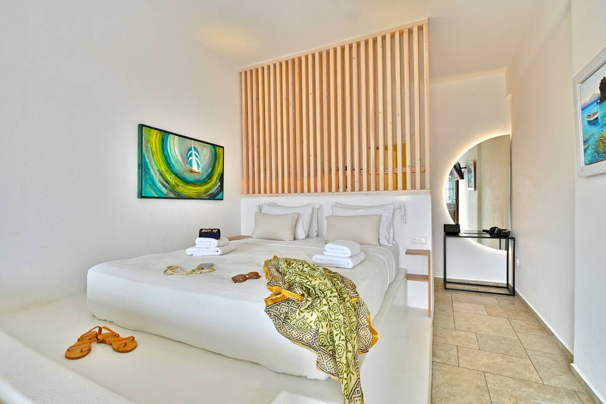 Une chambre d’hôtel moderne avec un grand lit, une tête de lit en lattes de bois, un tableau et un miroir.