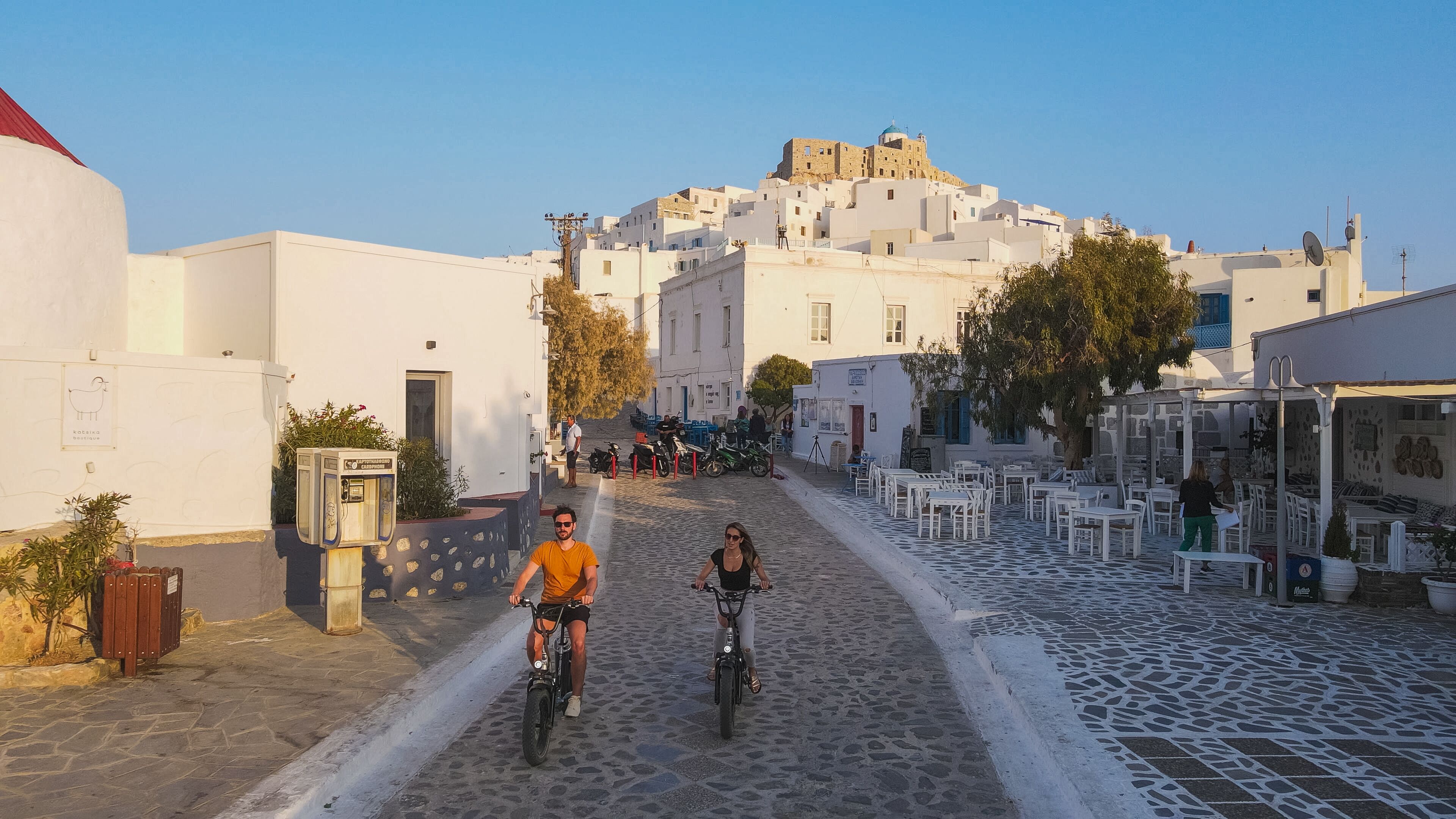 A cobblestone street leading to a hilltop building with white facades and blue domes.