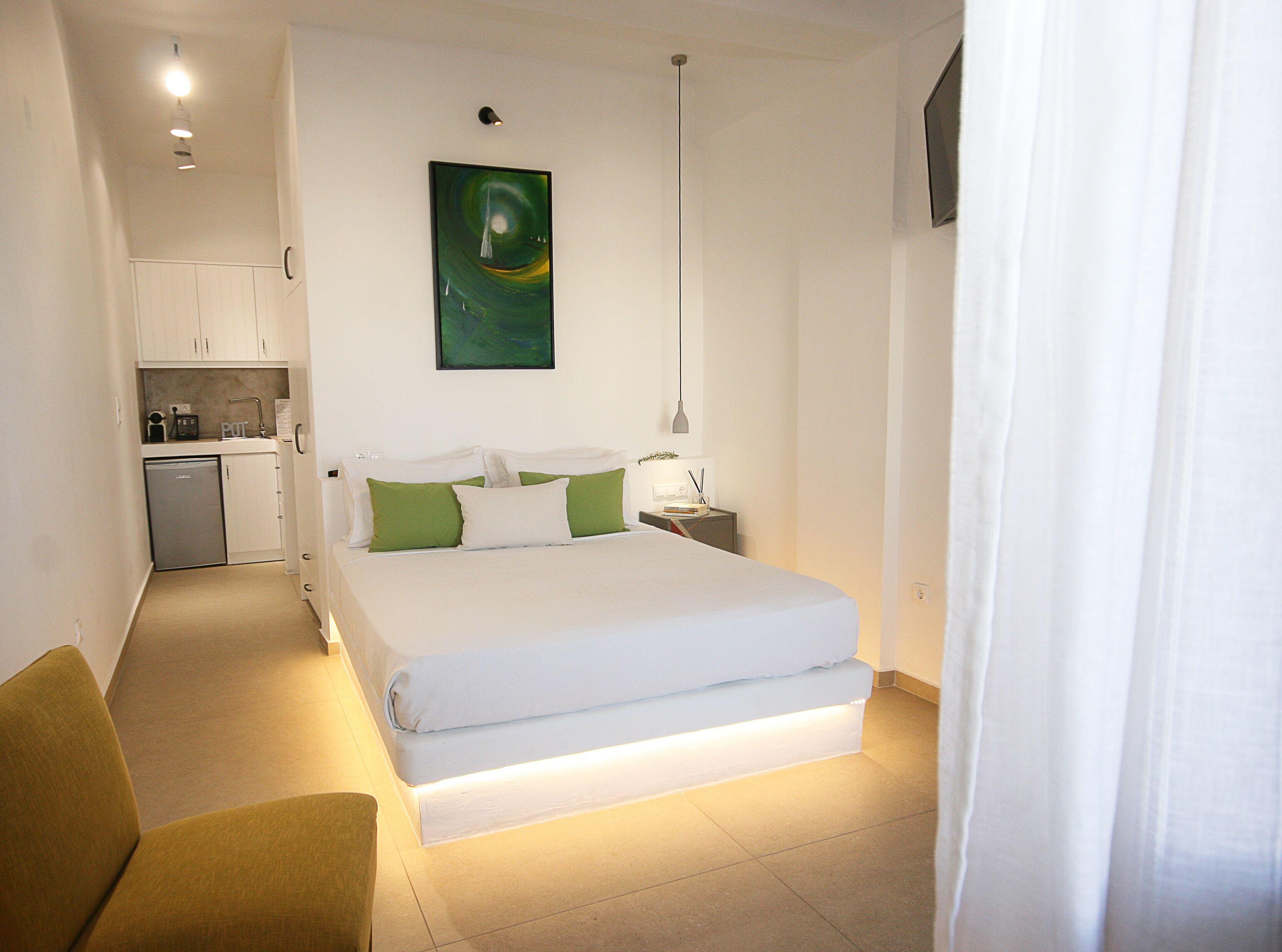 Une chambre d’hôtel de taille réduite, comprenant un lit, une table de chevet, une petite table d’appoint, un coin cuisine et une seule chaise.
