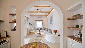 A modern kitchen with white cabinets, wooden countertops, and a dining area with a round table. - Kallichoron Art Hotel (Astypalaia)