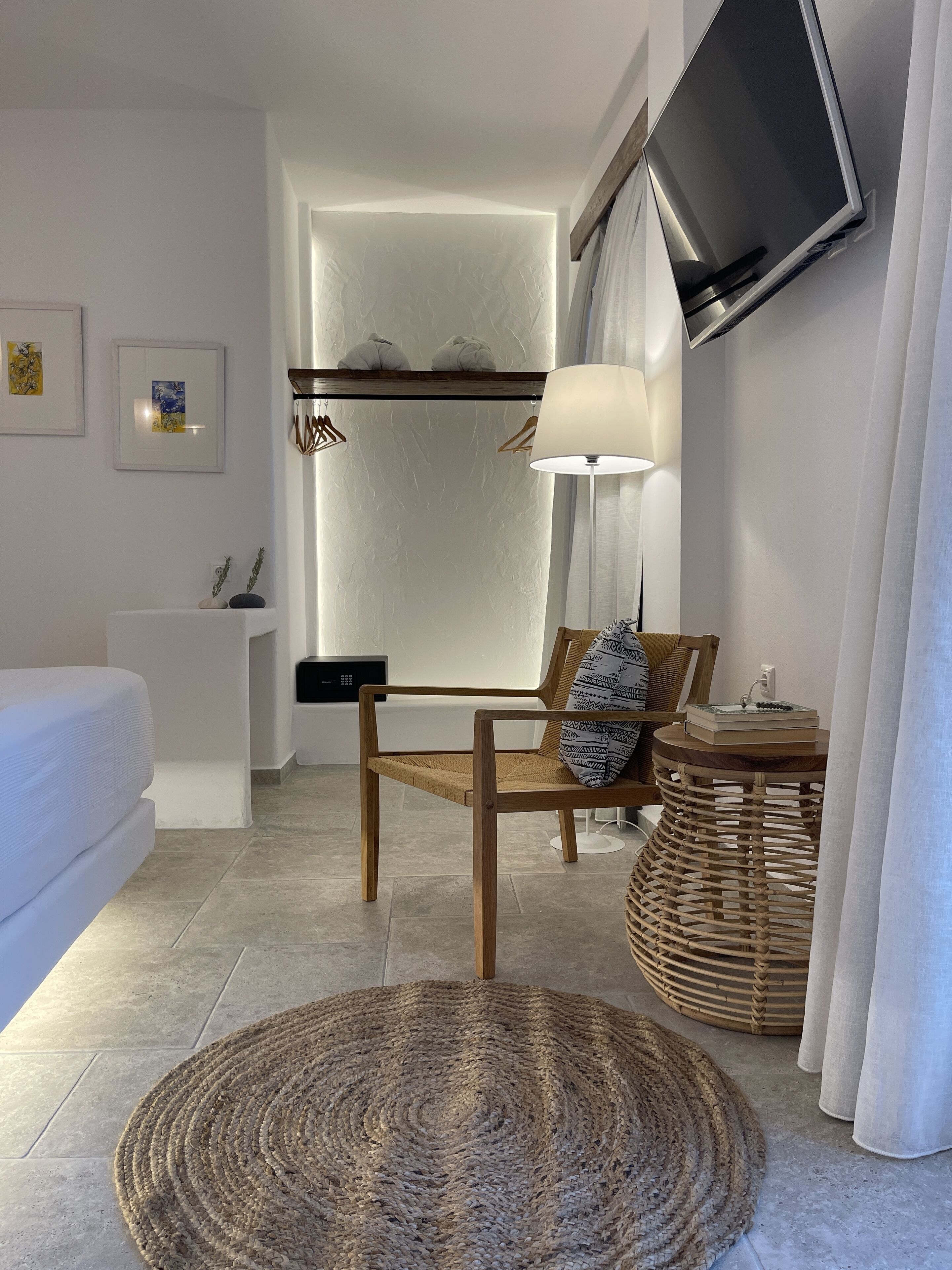 Un dormitorio moderno con una cama, una silla de madera, un tapete tejido, una mesita auxiliar, una lámpara y un televisor de pared.