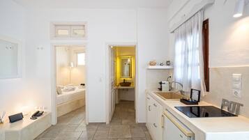 Een compacte hotelkamer met een bed, nachtkastje en een klein zithoekje. Het heeft een kitchenette met een spoelbak en kookplaat.
