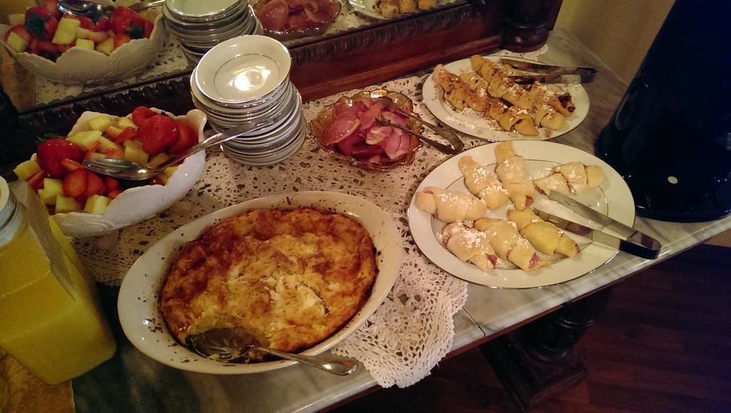 A buffet table with various dishes including a fruit bowl, a ham dish, and a pie.
