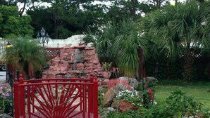 Ein rotes Tor in einem Garten mit einem kleinen Bach, umgeben von verschiedenen Pflanzen und einer Steinmauer.
