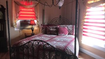 Une chambre à coucher avec un lit à baldaquin, une table de chevet avec une lampe, une fenêtre avec des stores et un climatiseur fixé au mur.