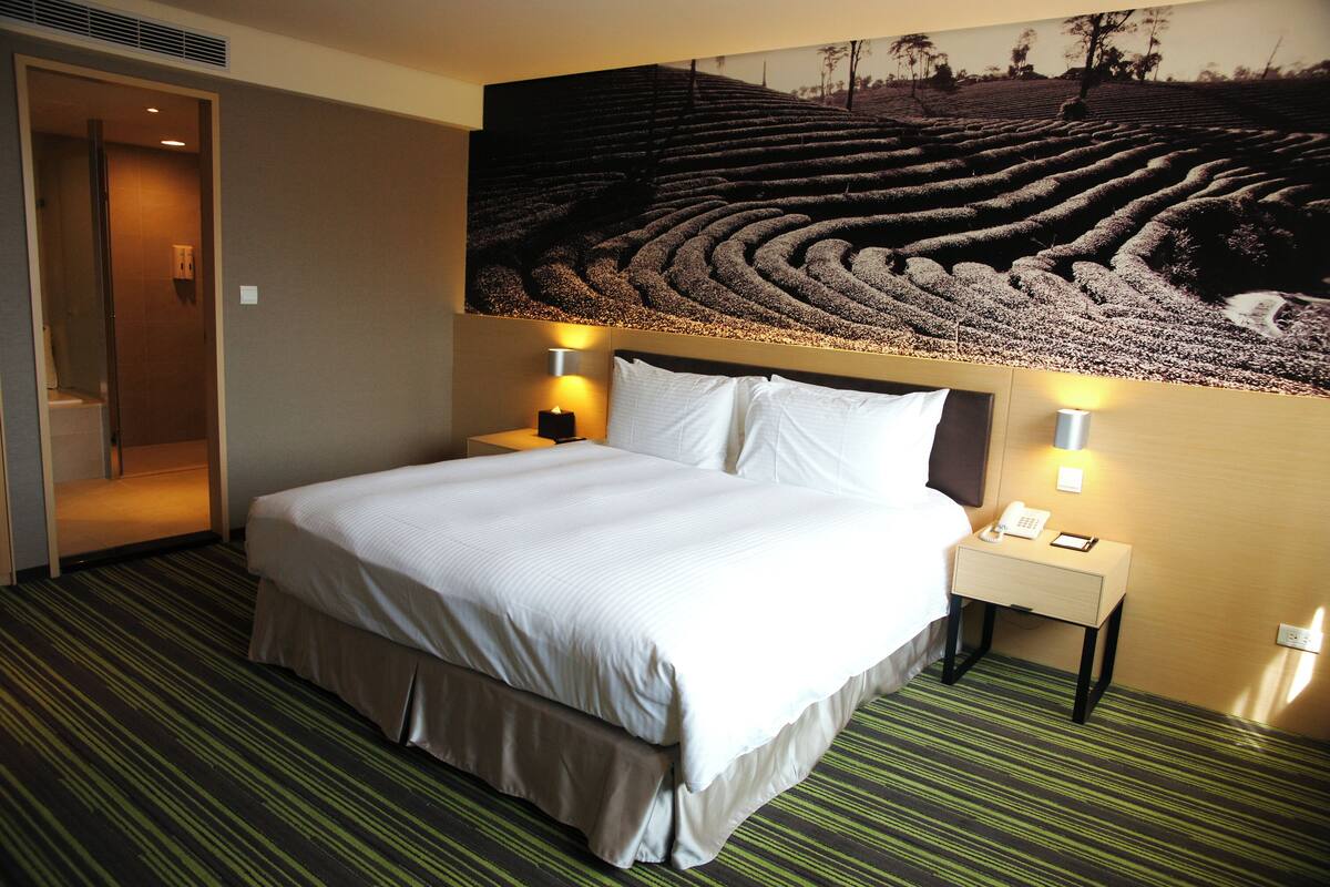 A hotel room with a large bed, two bedside tables with lamps, and a wall mural of a landscape.