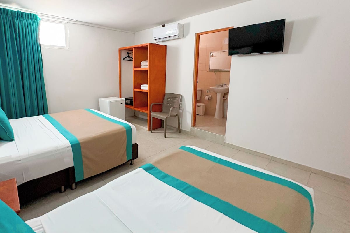 A hotel room with two beds, a wardrobe, a chair, a desk, and a bathroom visible through an open door.