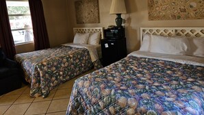 A hotel room with two beds, a window with curtains, a lamp, and artwork on the walls. - Captain's Cove Motel (Oak Island)