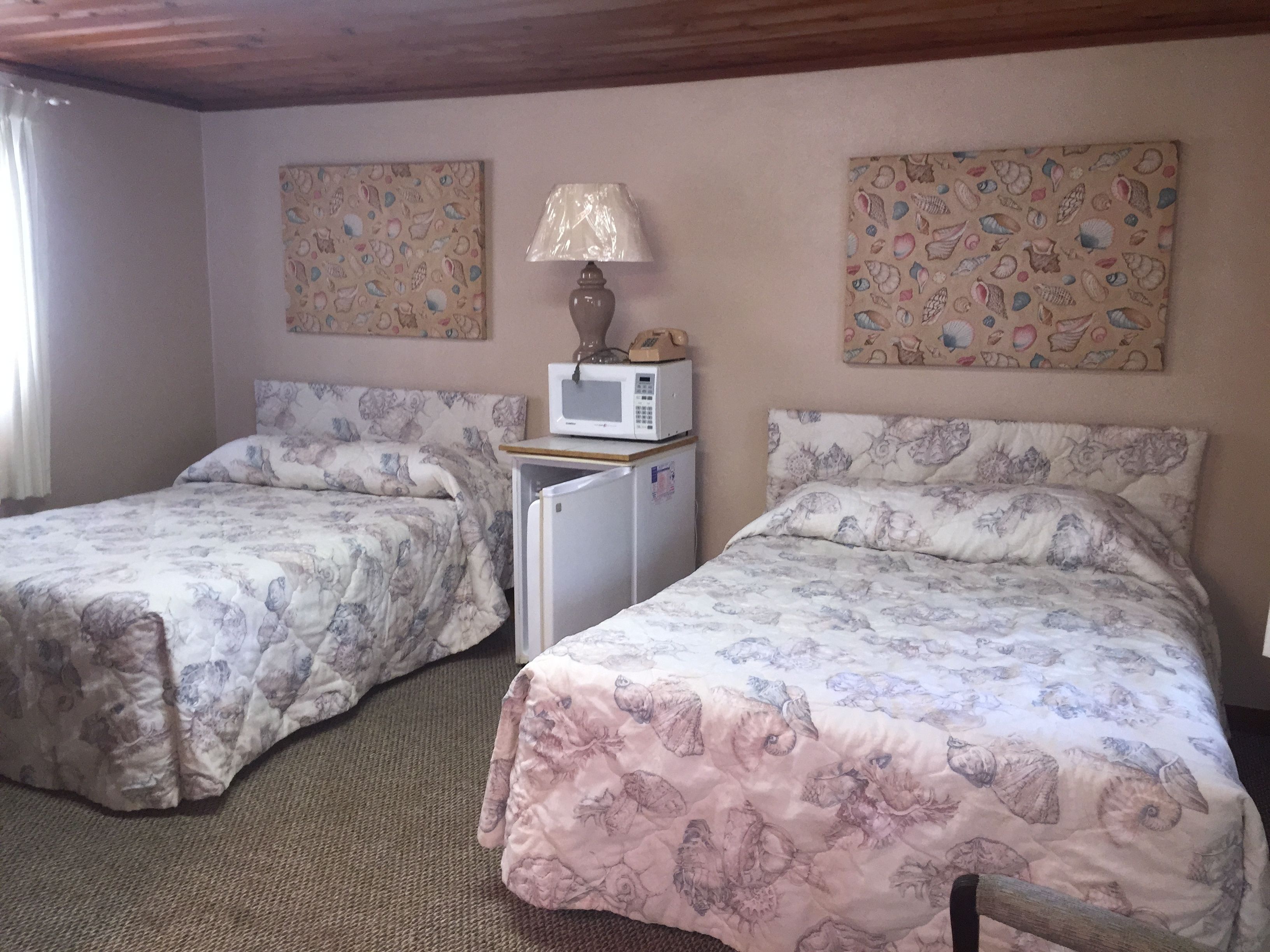 Ein Zimmer mit zwei Betten, jeweils mit blumigem Bettbezug, einem kleinen Kühlschrank, einer Mikrowelle und einer Lampe.