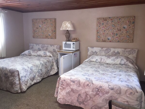 Una habitación con dos camas, cada una con ropa de cama estampada con motivos florales, un refrigerador pequeño, un microondas y una lámpara.