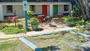 A building with a red door, a blue railing, and a barbecue area with potted plants. - Captain's Cove Motel (Oak Island)