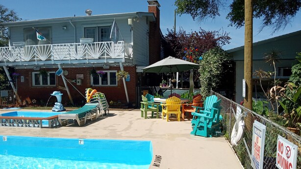 A pool area with lounge chairs, a small fountain, and a dining area with outdoor seating. - Captain's Cove Motel (Oak Island)
