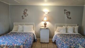 Une chambre avec deux lits, chacun recouvert d’une couvre-lit à motifs floraux, une petite table de chevet avec une lampe et des œuvres d’art décoratives accrochées au mur.