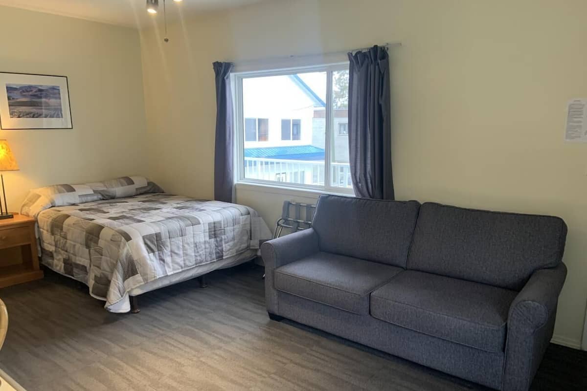 A room with a bed, a grey sofa, a lamp, and a window with curtains.