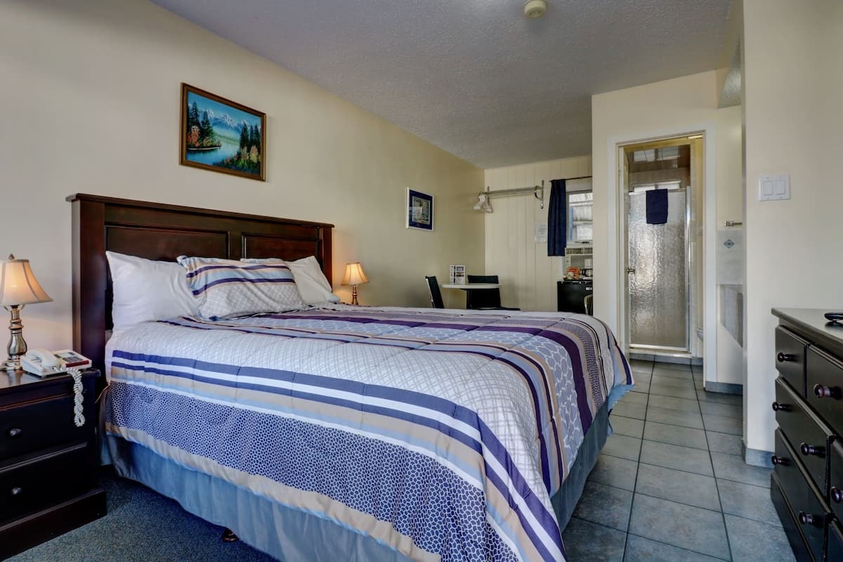 A hotel room with a large bed, a desk, a chair, a dresser, and a bathroom visible through an open door.