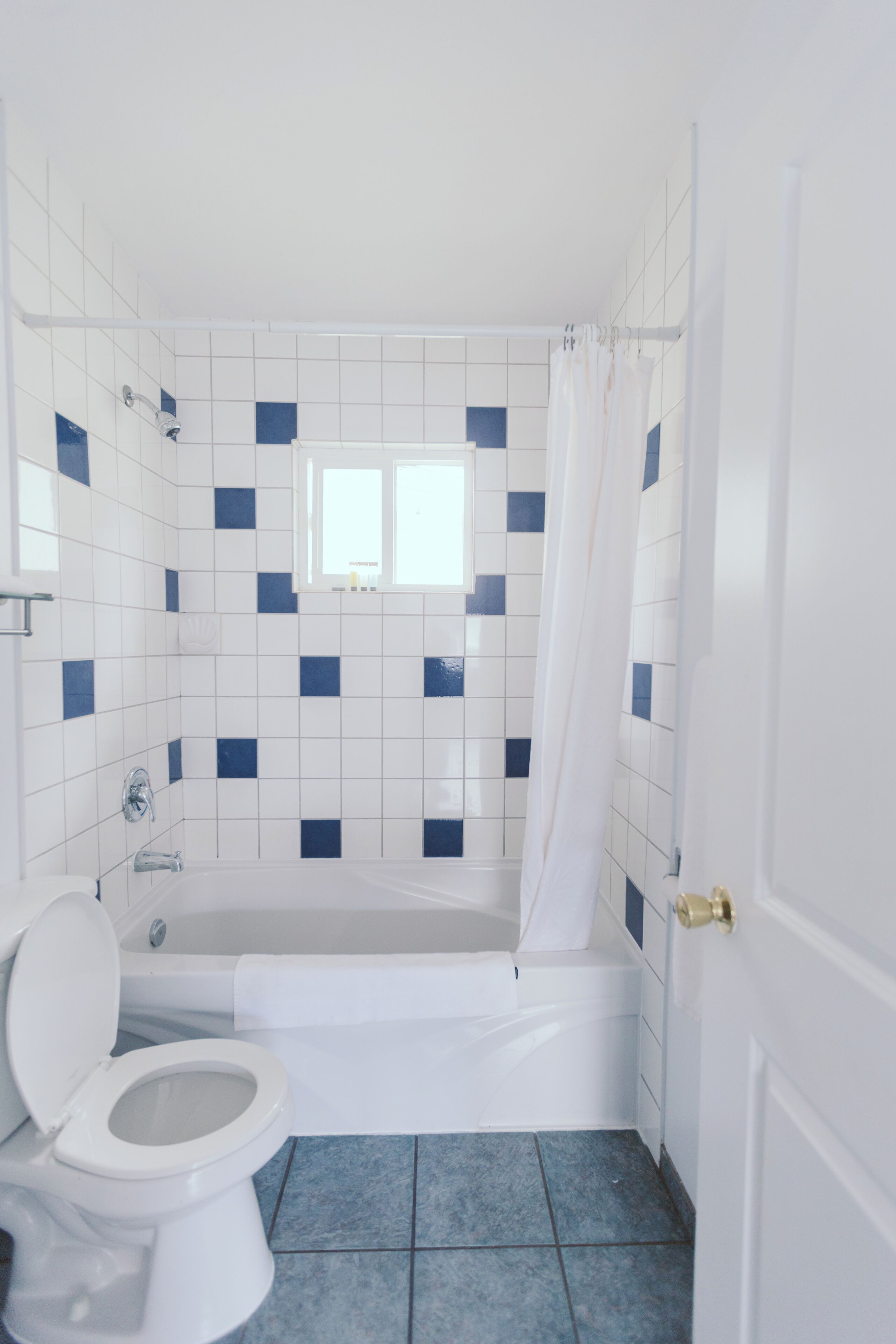 Une salle de bain avec une baignoire, des toilettes et une fenêtre située au-dessus de la baignoire.