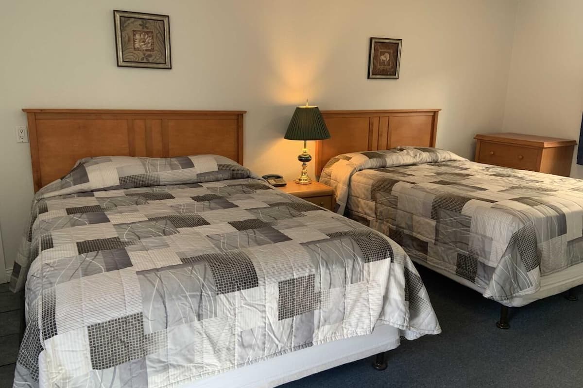 A hotel room with two beds, each with a quilted bedspread, a bedside table with a lamp, and a small wooden nightstand.