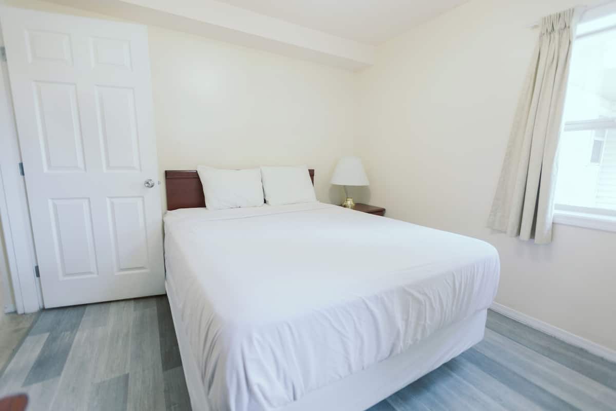 A bedroom with a large bed, a nightstand, a lamp, and a window with curtains.