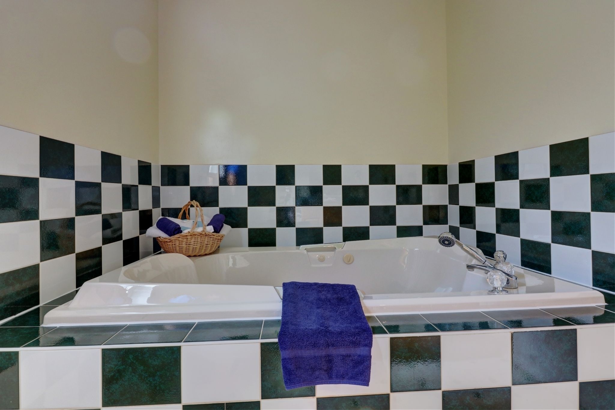 A bathroom with a checkered tile backsplash, a white bathtub, and a blue towel on the edge.