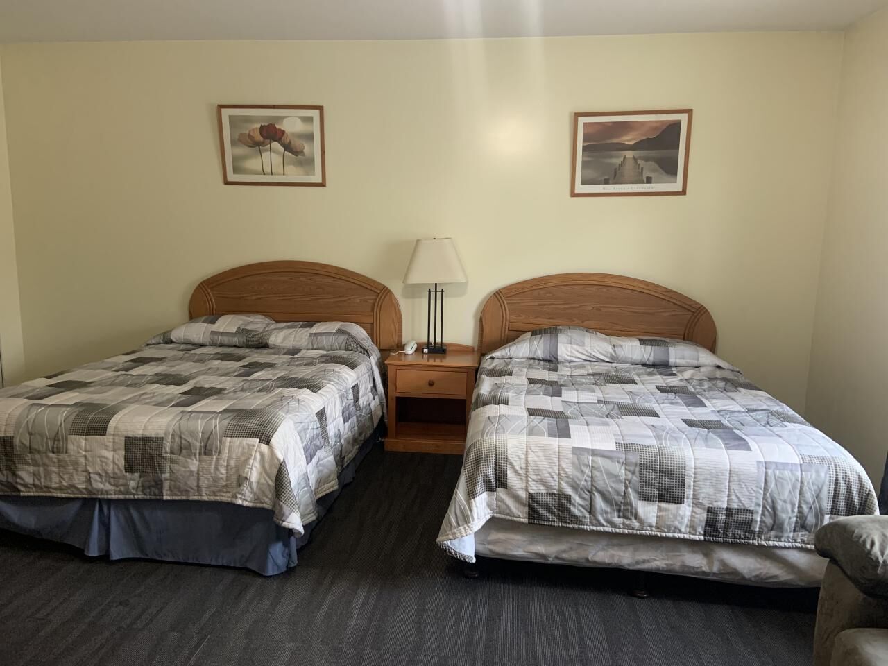 Habitación de hotel con dos camas individuales, una mesita de noche con lámpara y dos cuadros en la pared.
